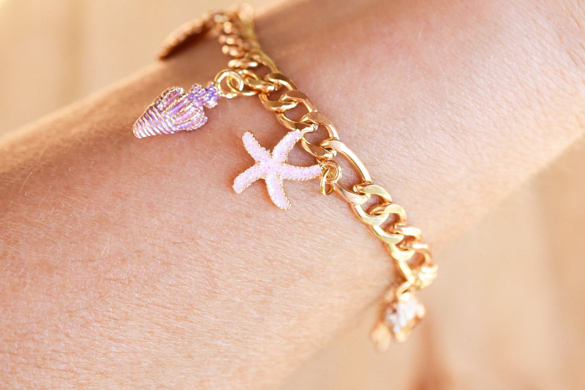 A gold chain charm bracelet with a starfish and shell charm on a woman's wrist