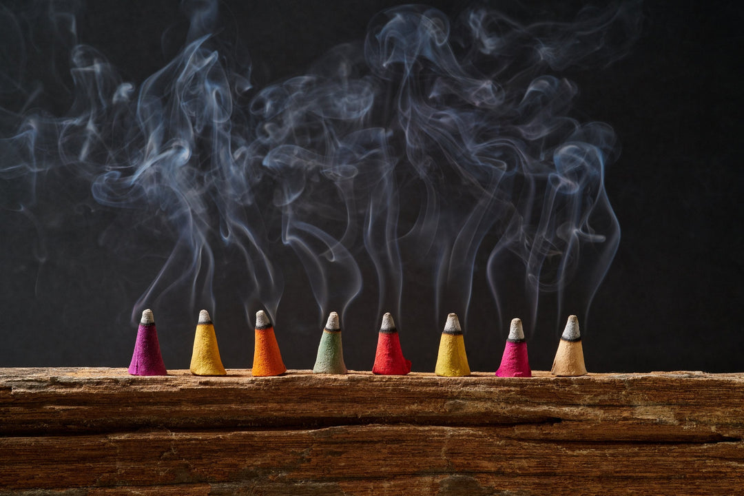 A row of coloured incense cones on old wood, with smoke curling up against a black background