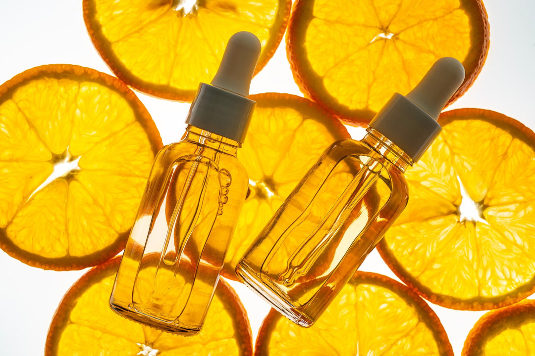 Vitamin C serum dropper bottles on backlit slices of orange