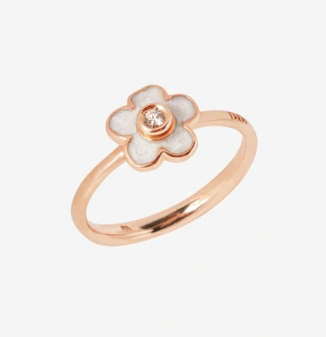 Rose gold floral ring with white enamel petals and a central diamond on neutral background